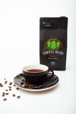 Pacote de café da da CrocBuds com uma xicara com café e grãos espalhados no fundo branco